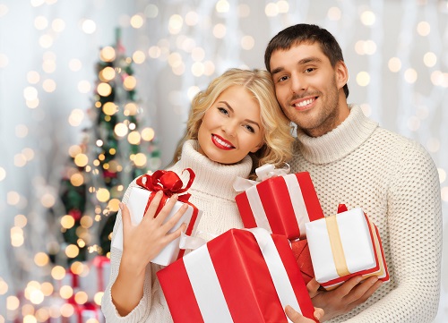 people, christmas, holidays and new year concept - happy family couple in sweaters holding gifts or presents over lights background