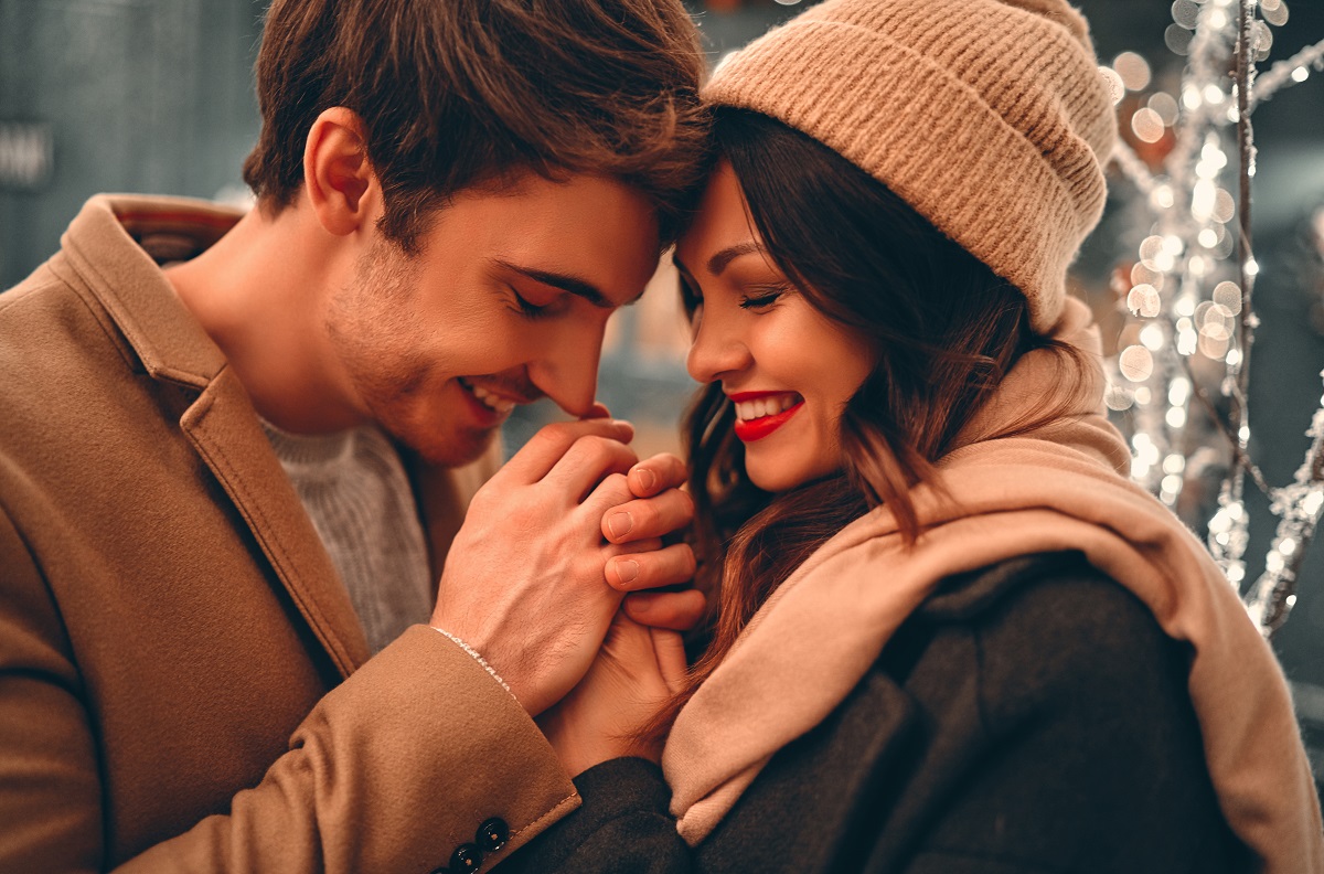 Young romantic couple is having fun outdoors in winter before Christmas. Enjoying spending time together in New Year Eve. Two lovers are hugging and kissing in Saint Valentine's Day.